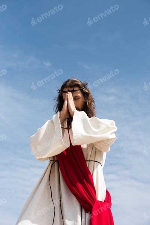 Preview: low angle view of Jesus Christ in robe, red sash and crown of thorns holding rosary and praying