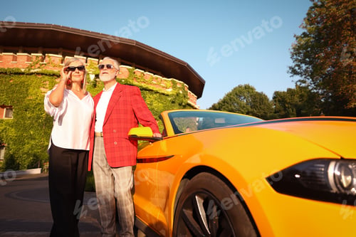 Preview: Stylish senior couple in sunglasses near modern cabriolet outdoors, low angle view