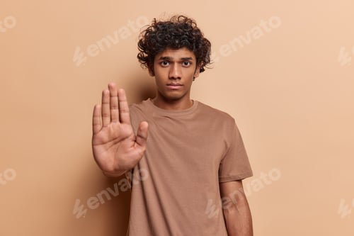 Preview: Waist up shot of curly haired Hindu man stretches out hand to block or refuse something shows stop