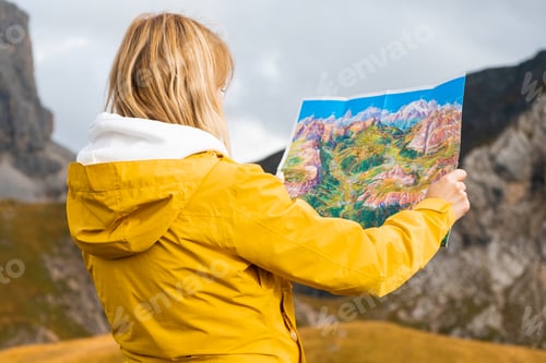 Preview: Back side of traveler woman searching the right way on the map in mountains,