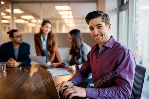 Preview: Happy businessman working on laptop during a meeting in the office and looking at camera.