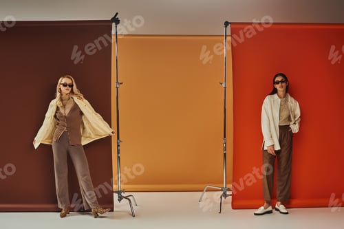 Preview: fall wardrobe, stylish multiethnic models in sunglasses and outerwear posing on colorful backdrop