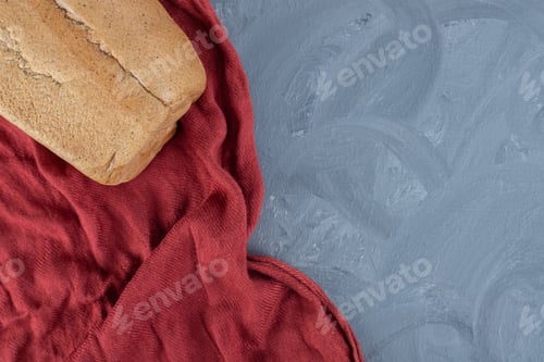 Preview: Block of bread on wrinkled red tablecloth on marble background
