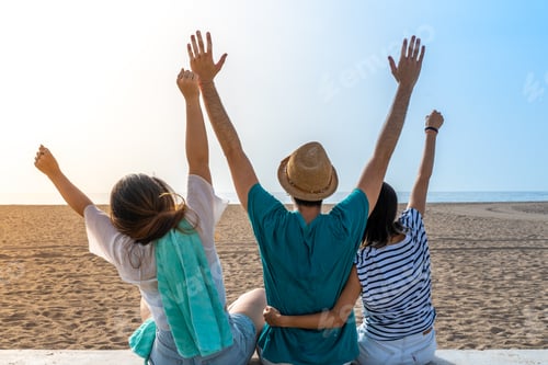 Preview: Happy friends holding each other in the beach with raised arms. Cheerful embracing each other, back