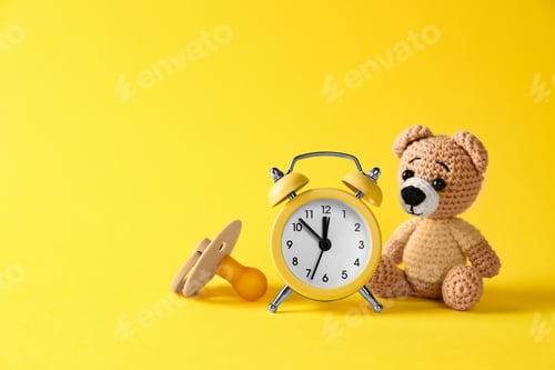 Preview: Alarm clock, toy bear and baby dummy on yellow background, space for text. Time to give birth