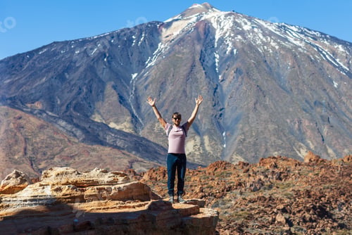 Preview: Happy man hiker standing on the edge of rock with raised hands