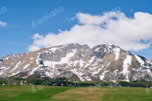 Preview: Green pasture near a small village at the foot of a mountain range covered with snow