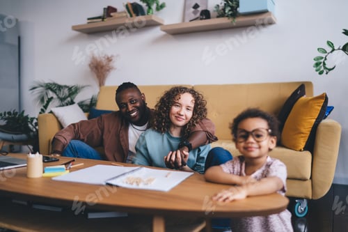 Preview: Cheerful multiethnic parent sitting together while looking at daughter at home