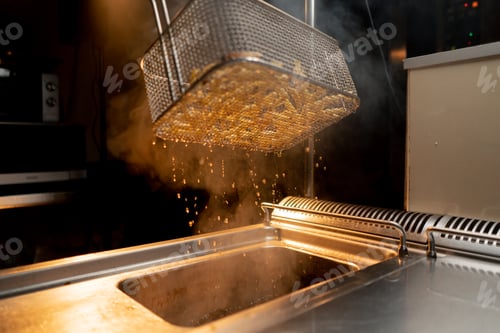 Preview: kitchen in the hotel restaurant the chef takes out delicious french fries from the fryer oil drips