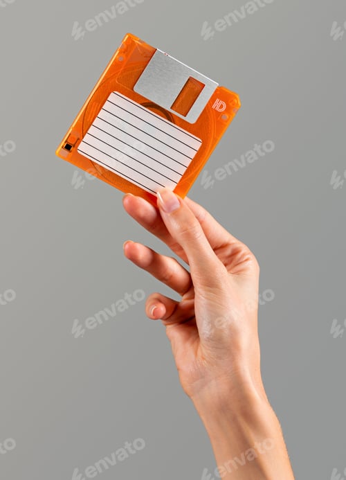 Preview: Unrecognizable woman displaying vintage floppy disk in light against gray backdrop