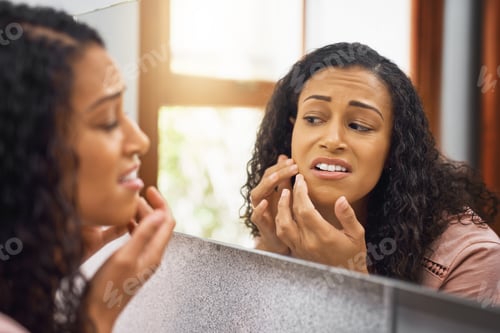Preview: Cropped shot of an attractive young woman examining her face in a mirror in the bathroom at home