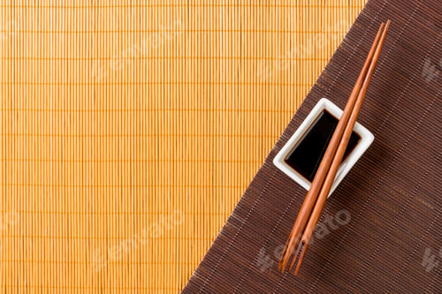 Preview: Chopsticks and bowl with soy sauce on two bamboo mat blak and yellow top view with copy space