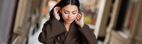 Preview: pretty brunette woman in brown coat fixing hair outdoors in prague, banner