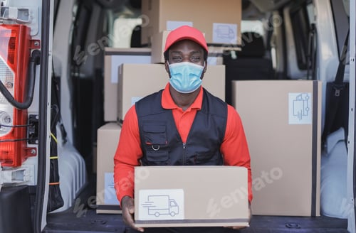 Preview: Young african delivery man holdign package while wearing safety face mask for coronavirus outbreak