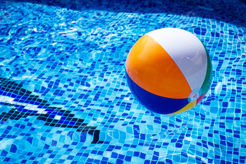 Preview: Colorful beach ball floats on the surface of a pool reflecting sunlight on a summer day