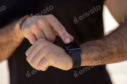 Preview: Unrecognizable man in fitwear uses smartwatch for workout monitoring outdoors