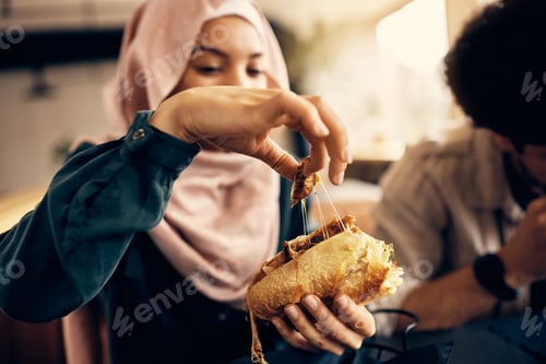 Preview: Close-up of woman having a sandwich while eating with friends in cafeteria.
