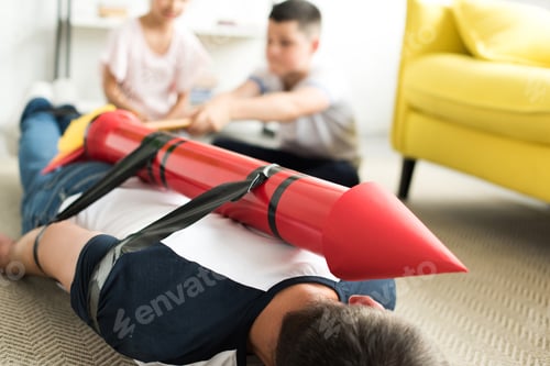 Preview: tied father with rocket toy lying on floor and children playing with him, parenthood concept