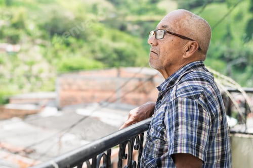 Preview: brown-skinned elderly latino man standing on the balcony of his house looking up at the sky