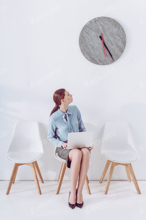 Preview: employee sitting on chair with laptop and looking at clock