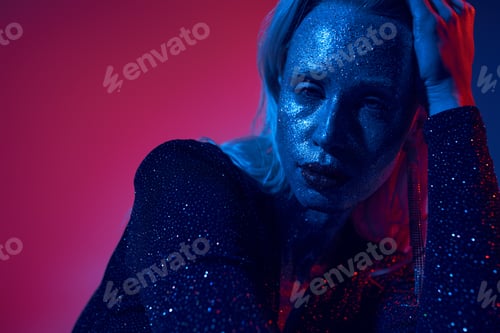Preview: portrait of pretty young woman with glitter on face and shiny outfit posing on neon background
