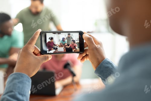 Preview: Hands of man with mobile phone filming multiracial male coworkers recording podcast in office