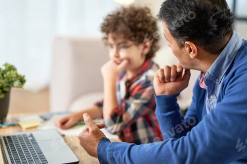 Preview: Latin middle aged father helping his cute son, school boy with studies while sitting at the table at