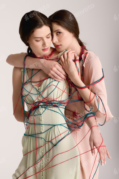 Preview: Twin sisters embrace each other in a creative fashion display with colorful threads