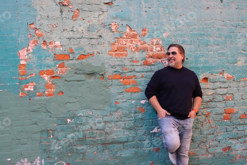 Preview: Man standing in front of blue brick wall and smiling