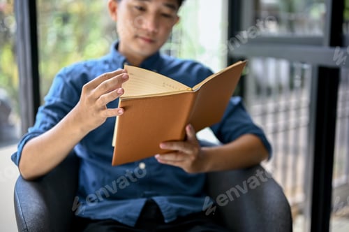 Preview: Close-up image, Happy Asian man reading a book while relaxing in a coffee shop.