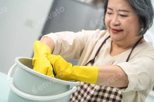 Preview: Asian young aged housewife twisting wet rag to clean the kitchen counter at home.