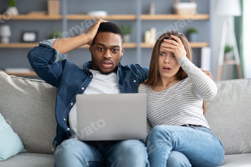 Preview: Shock Content. Frustrated interracial couple looking at laptop screen and touching heads