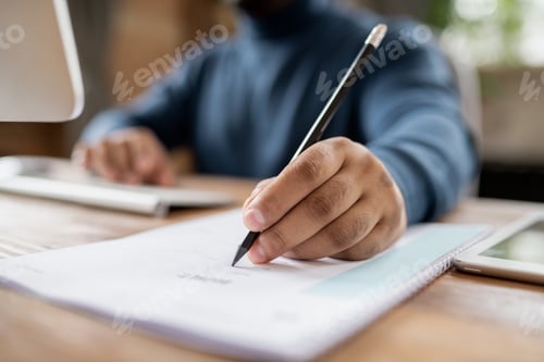 Preview: Hand of man holding pencil over document while sitting by table