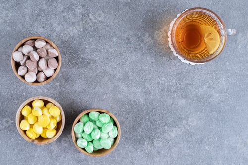 Preview: Delicious candies and cup of tea with lemon slice on marble surface