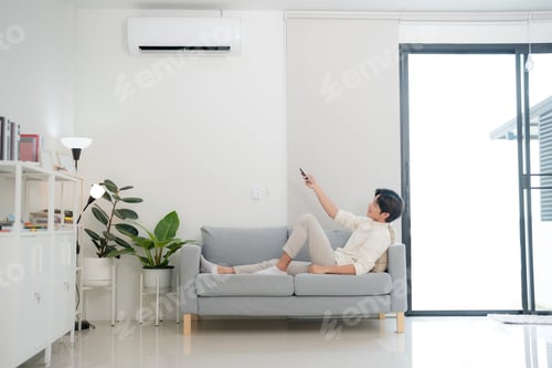 Preview: Young man enjoying comfort using remote control for air conditioning at home