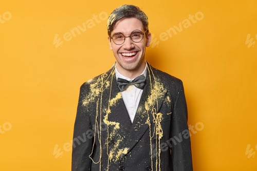 Preview: Cheerful adult man has fun on party smeared with serpentine spray smiles gladfully receives congratu
