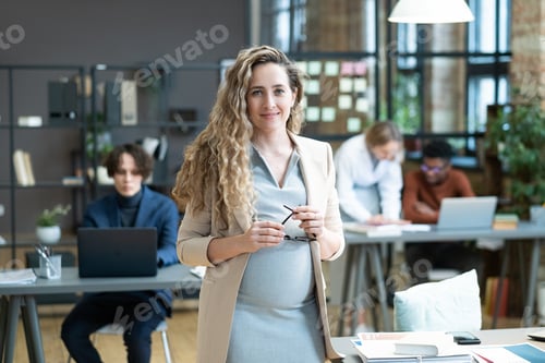 Preview: Happy young pregnant businesswoman in formalwear looking at you