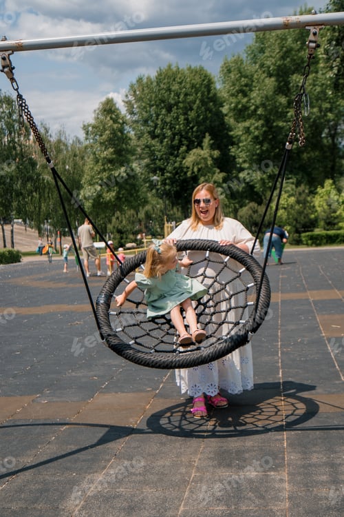 Preview: Little cute girl in a green summer dress with a bow on her head on the playground