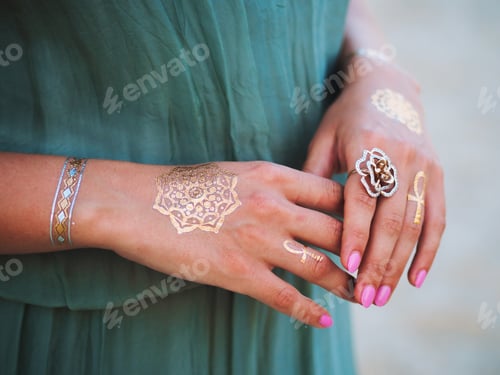 Preview: woman in green dress with boho gypsy accessories standing on beach demonstrates flash tattoos