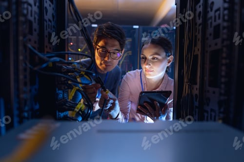 Preview: Diverse male and female engineers with digital tablet inspecting the server in computer server room