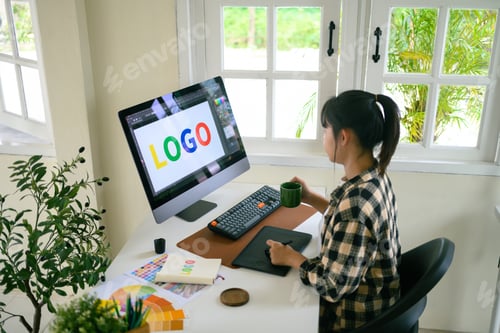 Preview: Graphic designer creating logo on digital tablet in bright modern workspace with computer