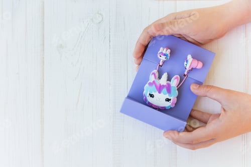 Preview: Packaged llama unicorn headphones for kids in purple pack in kids hands on white wooden background