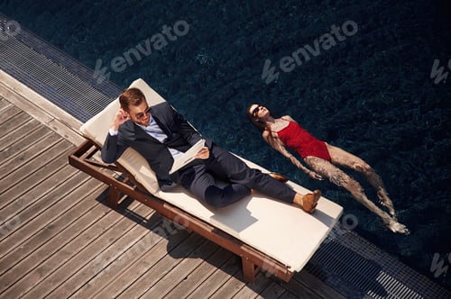 Preview: Business clothes, reading newspaper. Man with woman is in the pool together
