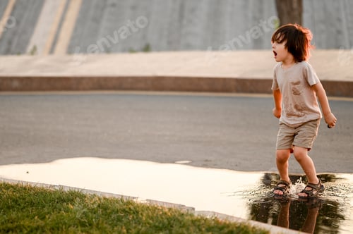Preview: A little boy cheerfully jumps through puddles in a summer park