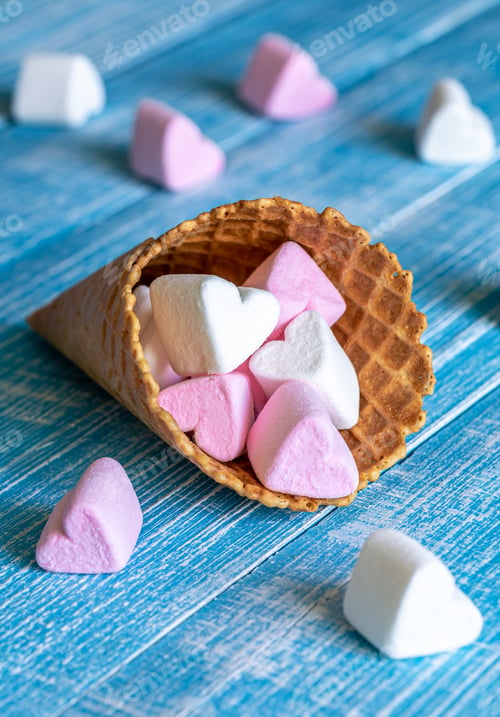 Preview: Waffle cone with heart-shaped marshmallows, close-up on a blue wooden background.