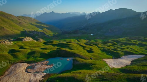 Preview: Scenic landscape of green hills, lake, and mountains under a clear blue sky.