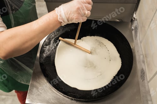 Preview: Chef prepares thin crepe in a kitchen using a flat skillet at a busy restaurant during