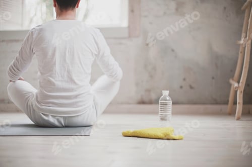 Preview: Candid authentic man millennial sitting in lotus pose and doing yoga in studio at home