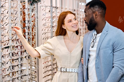 Preview: smiling kind beautiful female optician showing glasses to man
