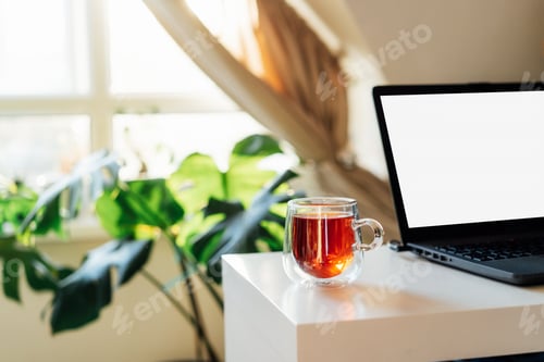 Preview: A home workplace with a white screen laptop for mockup and cup of tea on the table in sunset light